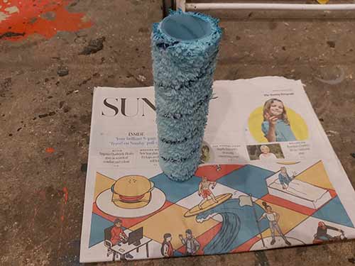 Paint roller standing up to dry on newspaper